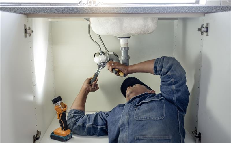Plumber repairing pipes beneath a bathroom sink in Cape Coral