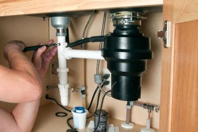 Plumber repairing a garbage disposal beneath a kitchen sink in Cape Coral