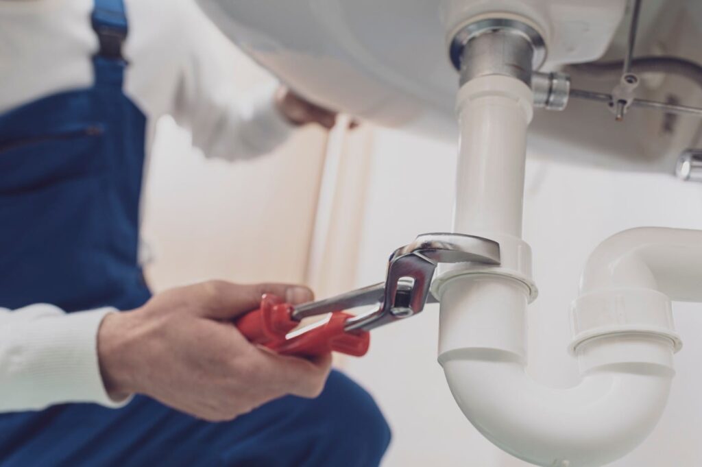 Plumber repairing a white drain pipe beneath a sink in Cape Coral