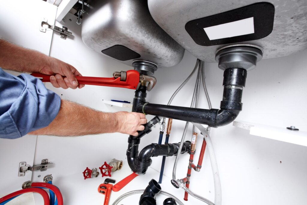 Plumber repairing drain pipes beneath a kitchen sink in Cape Coral